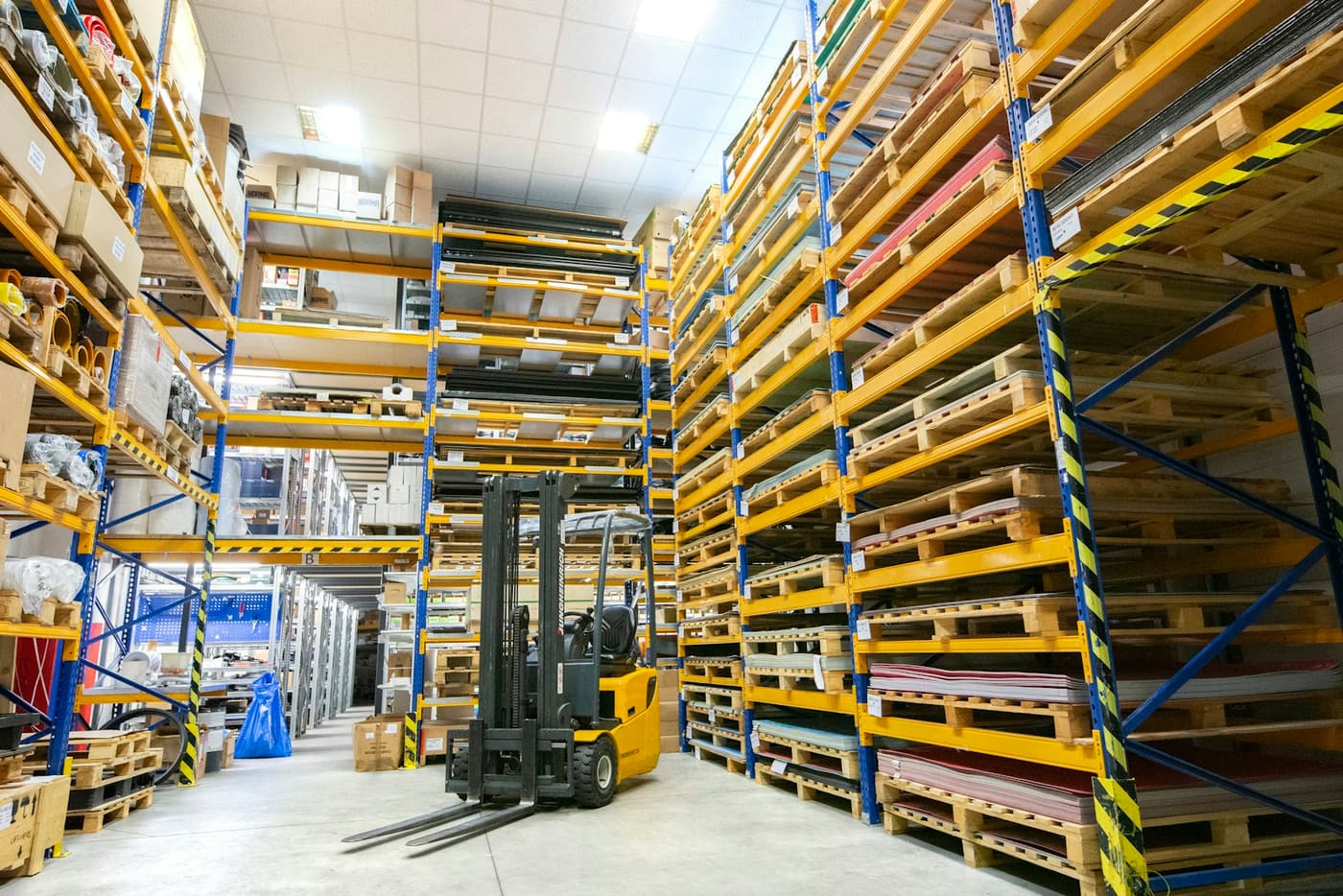 A forklift working between tall pallet racks in a warehouse.
