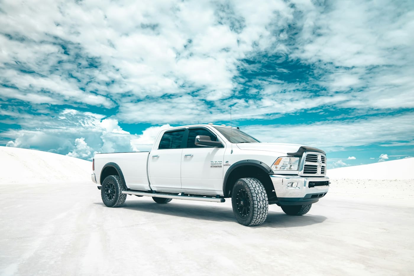 A white heavy-duty pickup parked on a flat expanse of snow under a bright sky.