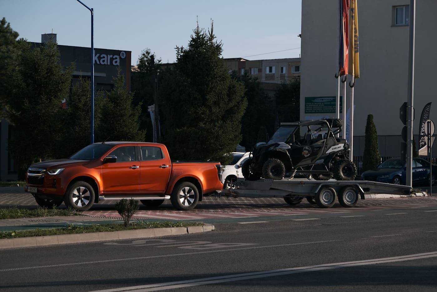 An orange pickup towing a trailer carrying a side-by-side utility vehicle.