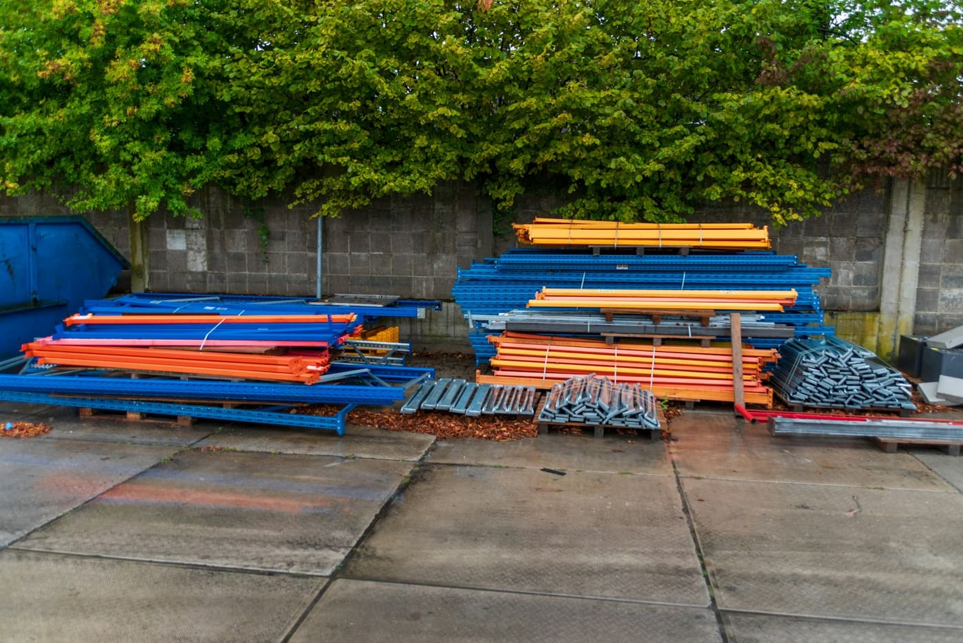 Painted scaffolding frames and shoring stacked against a wall on a site.