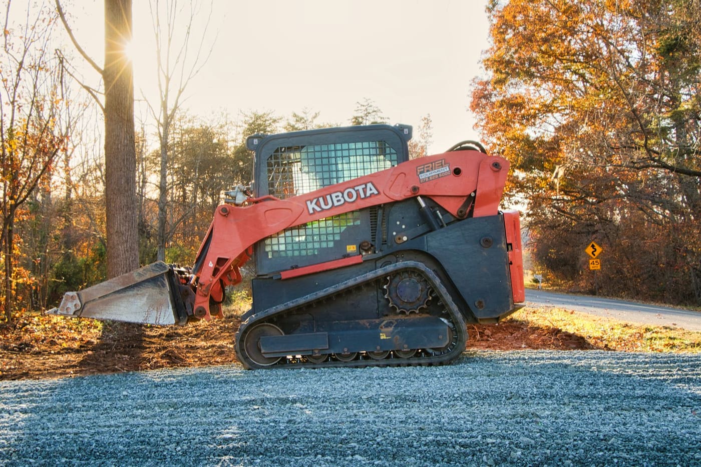 A compact track loader with its bucket lowered on a gravel road.
