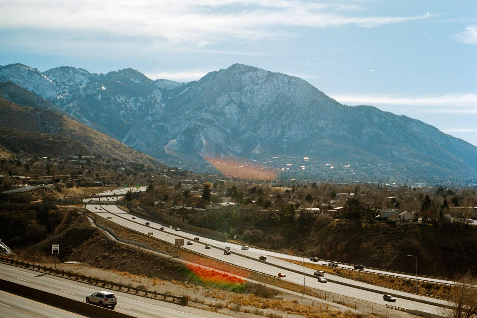 A multi-lane highway running through a valley with a high mountain range rising behind it.